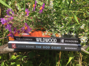 Purple and white wild flowers on top of the Dundurn books Wildwood and The God Game.