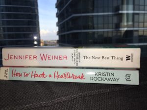 Spines of two books - The Next Best Thing and How to Hack a Heartbreak in front of condos