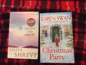 Two books Anita Shreve's Light on Snow and Karen Swan's The Christmas Party on a plaid red and black blanket