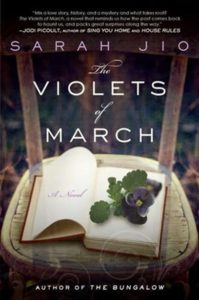 Front cover image of The Violets of March of purple violets on a book on a chair
